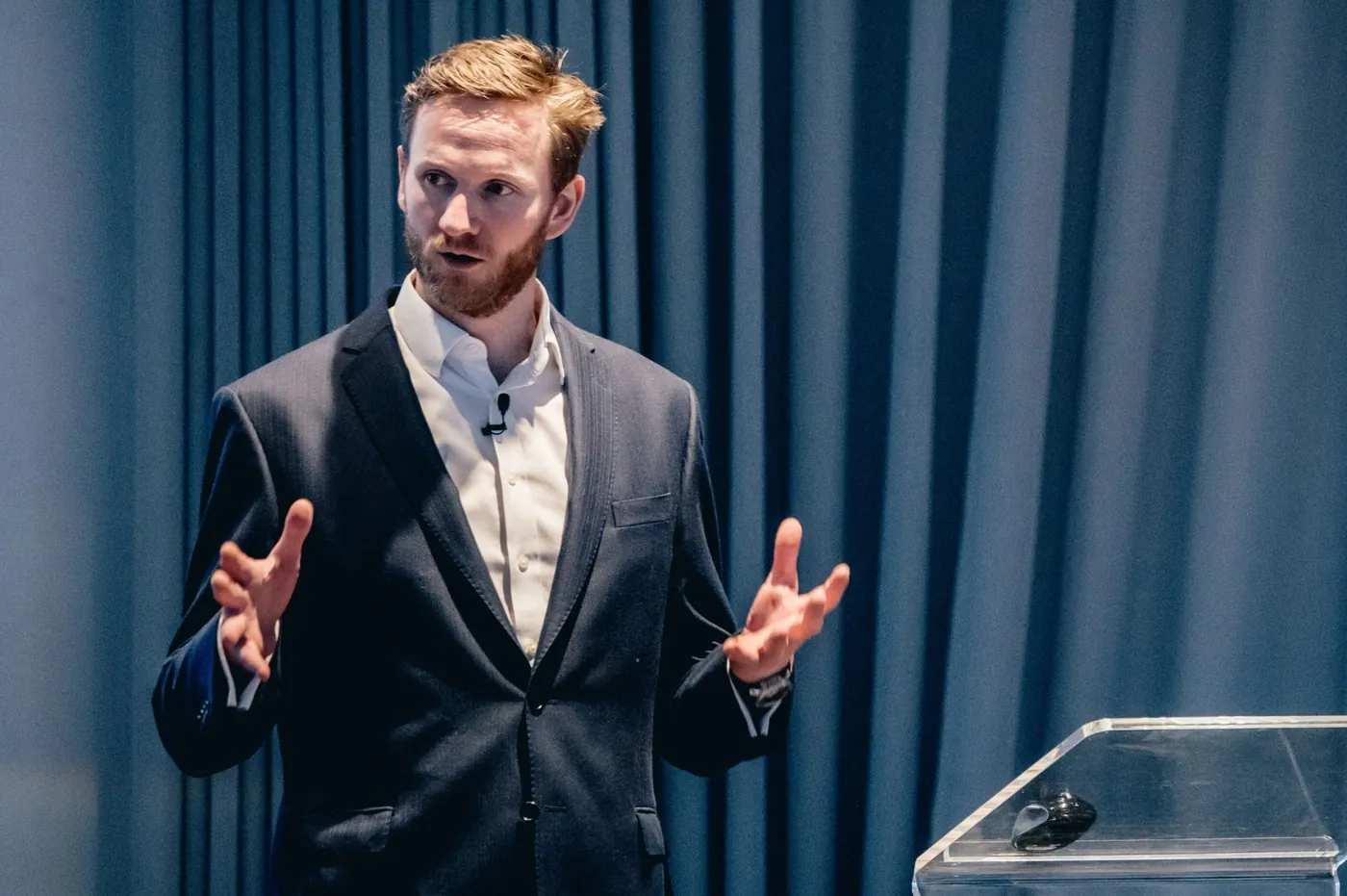 Mark Agnew delivering a keynote on stage in a dark suit, addressing a corporate audience